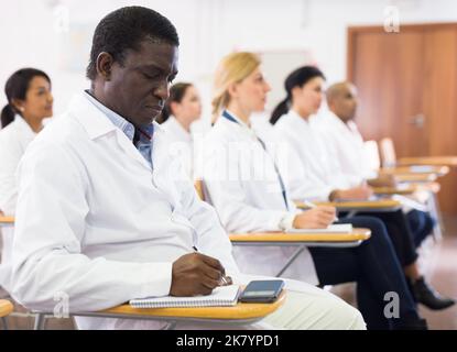African american man in white coat taking notes during lecture Stock Photo