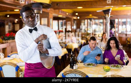 Tired african american waiter with empty serving tray in restaurant Stock Photo