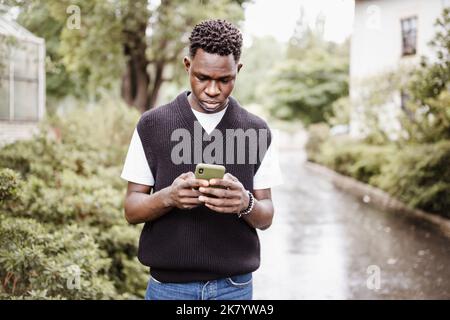 Young sad African American man in bomber jacket in park or street outdoor. Fall or spring season Stock Photo