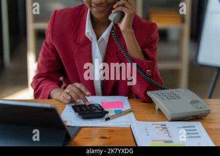 African American businesswoman using calculator and laptop for do math finance on wooden desk in office and business working background, tax Stock Photo