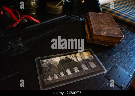 A photo of gravestones rests on a desk next to a warn leather bible at Cogswell's Grant in Essex, Massachusetts. Stock Photo