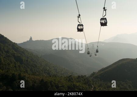 A cable car carries tourists to Ngong Ping Village and the Big Buddha, visible on the horizon on a hazy day, Lantau Island, Hong Kong Stock Photo