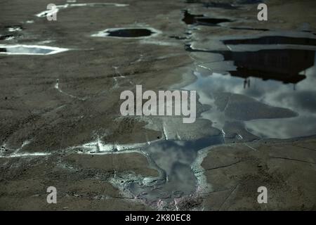 Big puddle in road. Reflection of sky in puddle. Water on asphalt. Large puddles after rain. Stock Photo