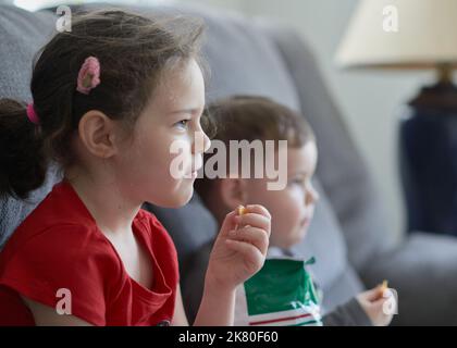 Brother and sister are eating chips and watching an amusing TV program Stock Photo
