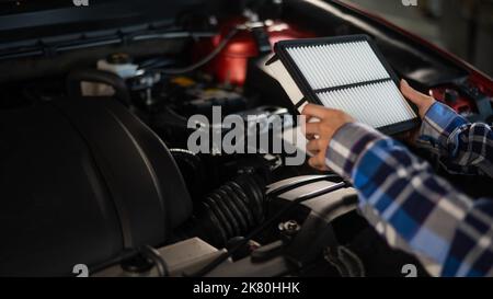 Caucasian female auto mechanic changes the engine air filter in the car. Stock Photo