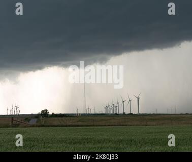 Menacing storm clouds over a wind farm in Oklahoma with a green crop in the foreground. Shallow depth of field. Stock Photo