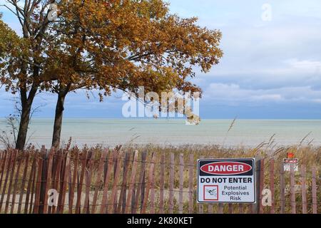Sign reads Danger Do Not Enter Potential Explosives Risk on a snow fence at Fort Sheridan in front of Lake Michigan in Illinois Stock Photo