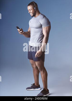 Getting my adrenaline from music. a handsome young man standing in the studio and listening to music through headphones while using his cellphone. Stock Photo