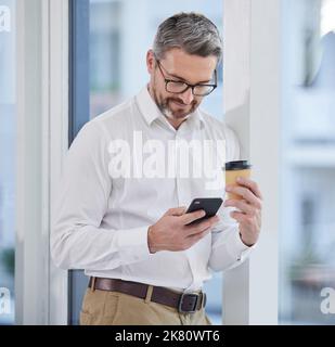This coffee is doing wonders. a businessman using his smartphone while drinking coffee. Stock Photo
