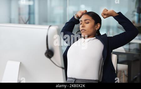 Its been a long day of making big sales. a young businesswoman stretching while working at her desk in a call centre. Stock Photo