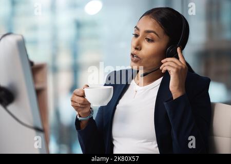 She knows how to sell a brand well. a young businesswoman drinking coffee while working on a computer in a call centre. Stock Photo