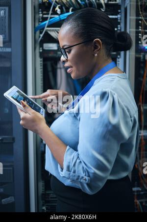 Getting the network to do what she wants. an attractive female programmer working on a tablet in a server room. Stock Photo