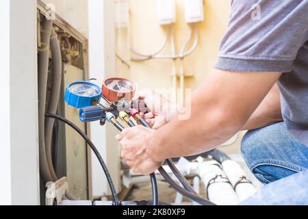 Air repair mechanic using measuring equipment for filling industrial factory air conditioners. Stock Photo