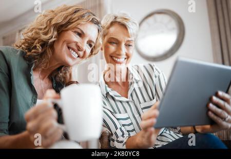 That video is hilarious. two female friends drinking coffee while using a digital tablet. Stock Photo