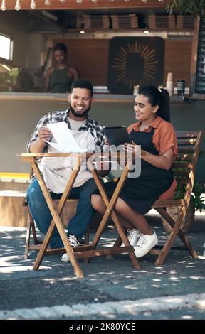 I have a few ideas we can work on. Full length shot of two young restaurant owners sitting outside together and using a digital tablet to plan their Stock Photo