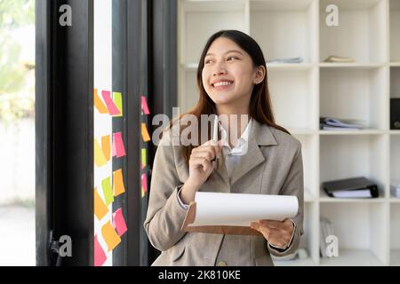 Portrait smile young asian woman making decisions thinking while at the office window. Stock Photo