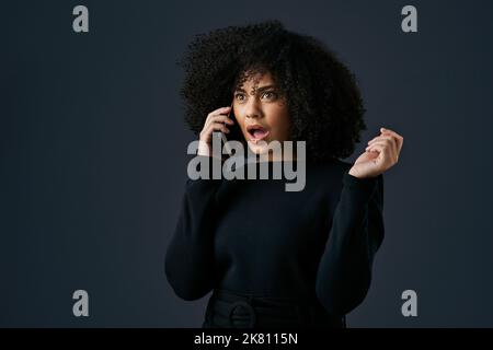 You have to fill me in on the gossip. a young businesswoman using her smartphone against a studio background. Stock Photo