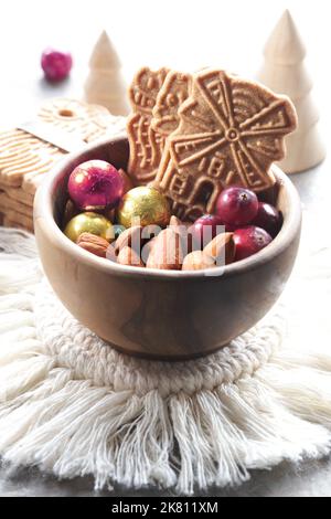 Speculoos or Spekulatius, Christmas biscuits, chocolate balls and almonds in wooden bowl. Winter snacks on a table with wooden Xmas tree toys Stock Photo