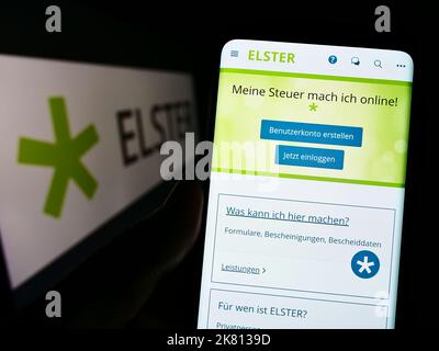 Person holding smartphone with webpage of German tax software Elster on screen in front of logo. Focus on center of phone display. Stock Photo