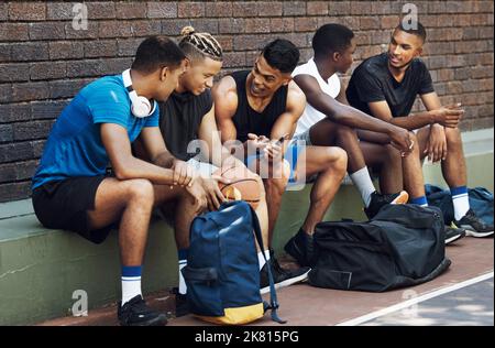 Basketball, sports and phone with a team talking on a court bench after a game or match outdoor. Teamwork, technology and conversation with a man