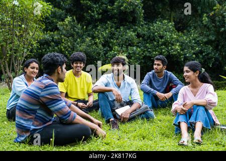 Group of happy students having chat with each other while sitting on college campus park - concept of takng break, communication and development. Stock Photo