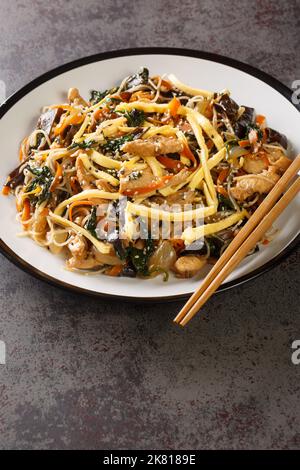 japchae or stir-fried Korean vermicelli noodles with vegetables and pork topped with sesame closeup on the plate on the table. Vertical Stock Photo