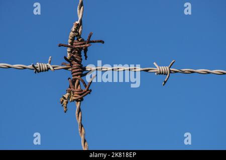 Interlinked barbed wire forming a cross against a blue sky Stock Photo