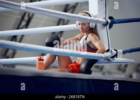 Young female athlete, professional boxer, kickboxer have a rest after hard training at sports gym. Concept of sport, workout, active and healthy Stock Photo