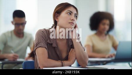 Theres something lethally charming about the daydreamers. a university student lost in thought in a classroom of university students. Stock Photo