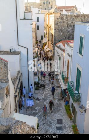 Via Immacolata, a narrow, paved street in Otranto with small shops and restaurants and people walking seen from a height. Apulia (Puglia), Italy. Stock Photo