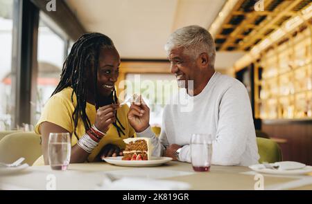 Happy senior couple smiling at each other while sharing a delicious cake in a cafe. Carefree senior couple having a good time in a restaurant. Mature Stock Photo