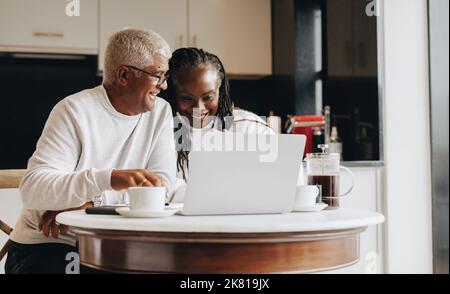 Happy senior couple having a video call on a laptop at home. Mature couple having a virtual meeting with a retirement consultant. Ethnic senior couple Stock Photo