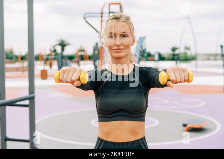Young athletic woman doing exercises with dumbbells on the sports ground. Stock Photo