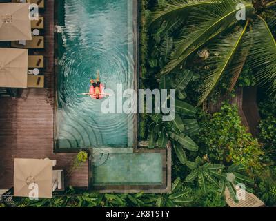 Aerial view of luxury resort with man on inflatable ring in pool. Top view of hotel surrounded with trees. Stock Photo