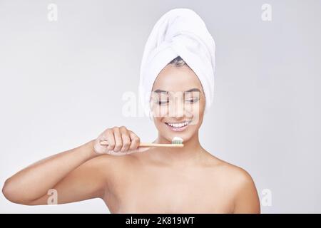 Hygiene is the new black. Studio shot of a beautiful young woman brushing her teeth against a grey background. Stock Photo