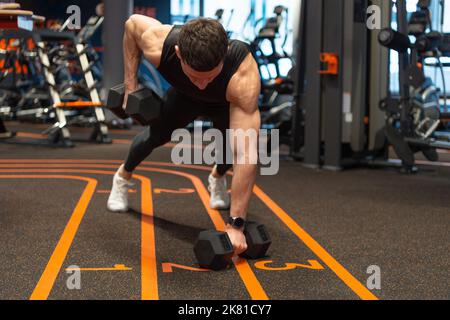 Athlete planking with dumbbells in fitness gym. Athletic man doing gym dumbbell plank row Stock Photo