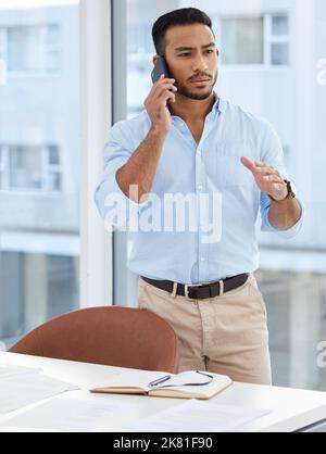 He gets things done a certain way. a young businessman talking on a cellphone in an office. Stock Photo