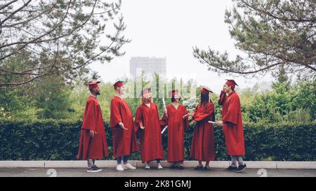 happy graduates laughing and celebrating graduation on college campus. Education, success and modern youth concept. Stock Photo