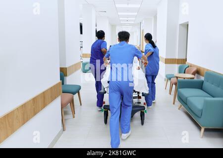 hospital care team wheeling patient on medical gurney at emergency department of hospital, back view Stock Photo