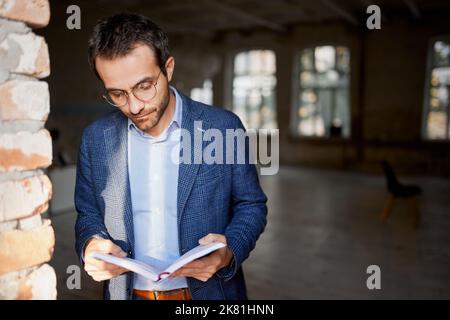 Portrait of businessman standing at the wall in empty room, making notes, working on new company opening Stock Photo