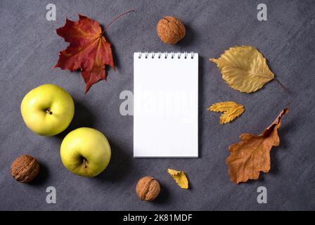 Autumn composition of dry leaves, apples, walnuts white notepad. Stock Photo