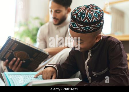 Like father, like son. a young muslim man and his son reading in the lounge at home. Stock Photo