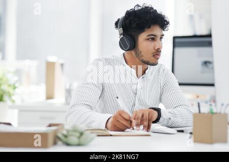 Prepping for some big plans. a young businessman writing notes while working on a computer in an office. Stock Photo