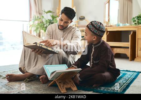 Your child will not depart from his teaching. a young muslim man and his son reading in the lounge at home. Stock Photo