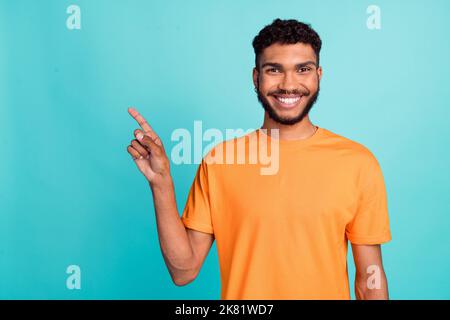 Photo of sweet good mood man dressed orange t-shirt pointing finger empty space isolated turquoise color background Stock Photo