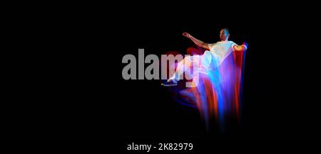 In miracle flight. Young sportive dancer in white clothes levitating, moving over dark background in mixed neon light. Creative art, aspiration, music Stock Photo