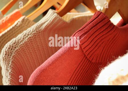 Warm sweaters on a wardrobe hanger on a light background. Autumn, winter clothes Stock Photo