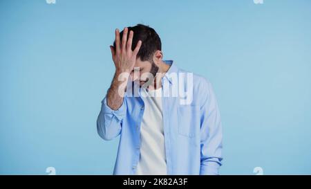 displeased bearded man in shirt touching head with hand isolated on blue Stock Photo