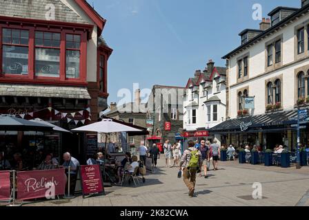 People tourists visitors walkers eating drinking at restaurants cafe and shops in the town centre in summer Main Street Keswick Cumbria England UK Stock Photo