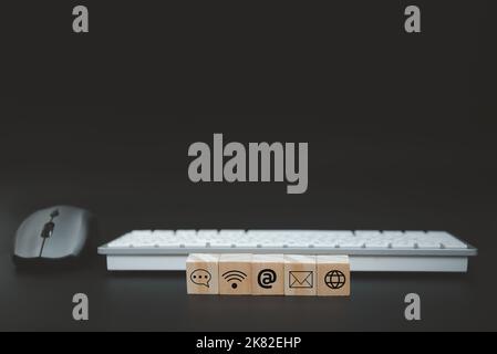 Online business communication symbols contact us or e-mail address marketing concept on wooden cubes with computer keyboard background. Stock Photo
